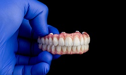 A gloved hand holding implant dentures