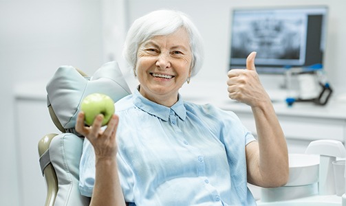 Older woman with dentures smiling and holding an apple