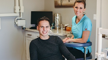 Young man and dental team member smiling after orthodontic treatment visit