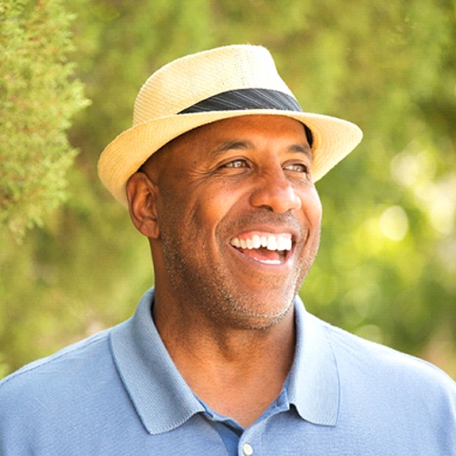 man wearing fedora and blue polo and smiling with dental bridges in Idaho Falls
