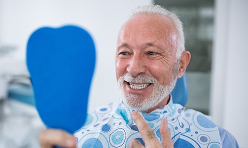 Man looking at denture in hand mirror