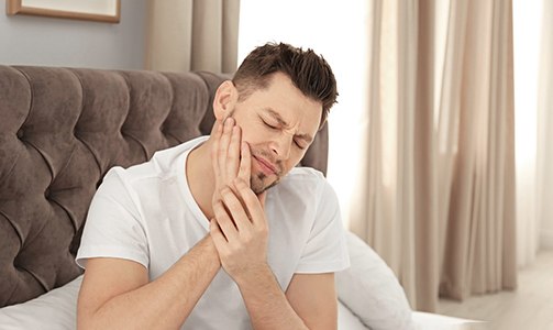 Man sitting in bed rubbing jaw in pain