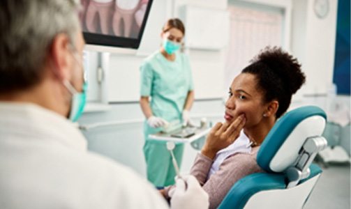 Woman looking at emergency dentist while holding cheek due to tooth pain