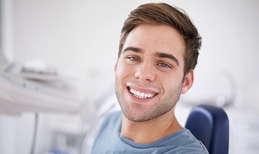 Man in dental chair smiling after teeth whitening